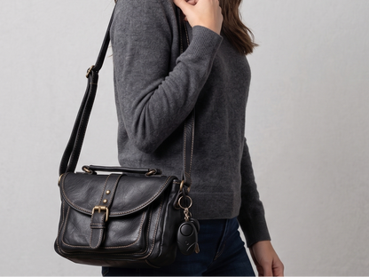 Person wearing a dark grey sweater with a black leather satchel bag with a SafeHer alarm clipped on with a light grey background